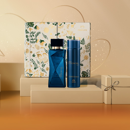 Itens da linha Essencial Oud, Deo Parfum e Óleo Corporal Perfumado, em fundo com caixa de presente floral sobre presente na cor creme com laço. Frascos azuis.