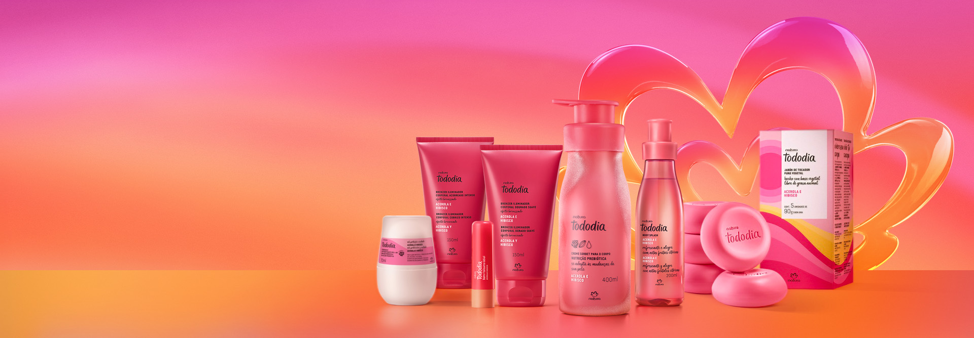 Tododia Acerola e Hibisco, em rosa: Desodorante Roll-On, bisnagas de tons de Iluminador, com Balm Labial, frascos de Creme Sorbet e de Body Splash e Sabonetes em Barra com caixa em fundo rosa e laranja com flor Natura em rosa e laranja.