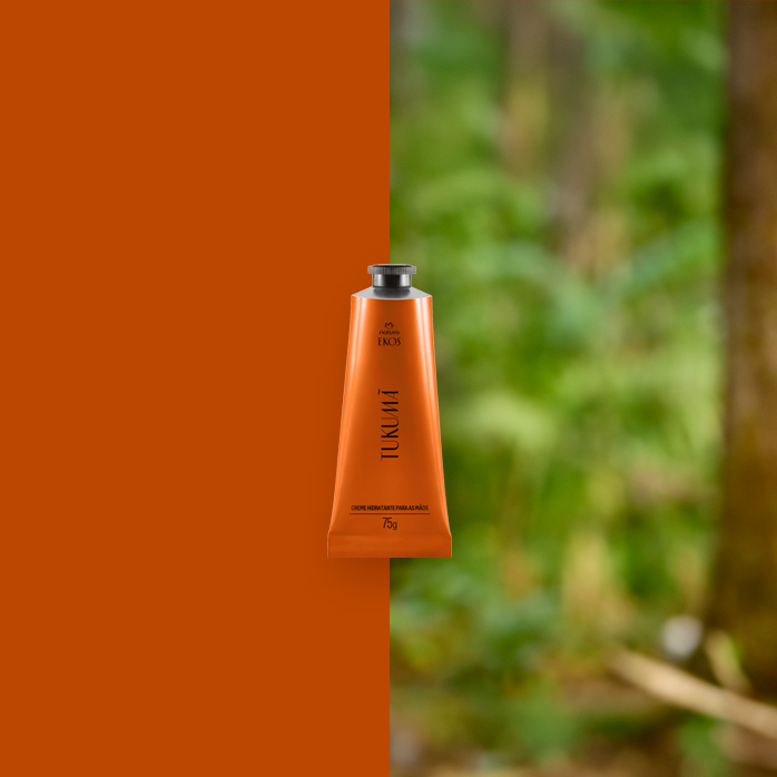 Bisnaga laranja do Creme Hidratante para as Mãos Ekos Tukumã centralizada, com fundo dividido entre laranja sólido e floresta desfocada ao fundo.