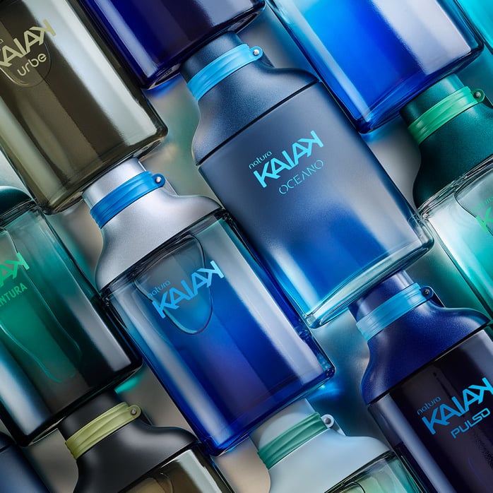 Frascos de diferentes fragrâncias Kaiak, em diversos tons de azul e verde. Itens em diagonal sobre um fundo prateado.