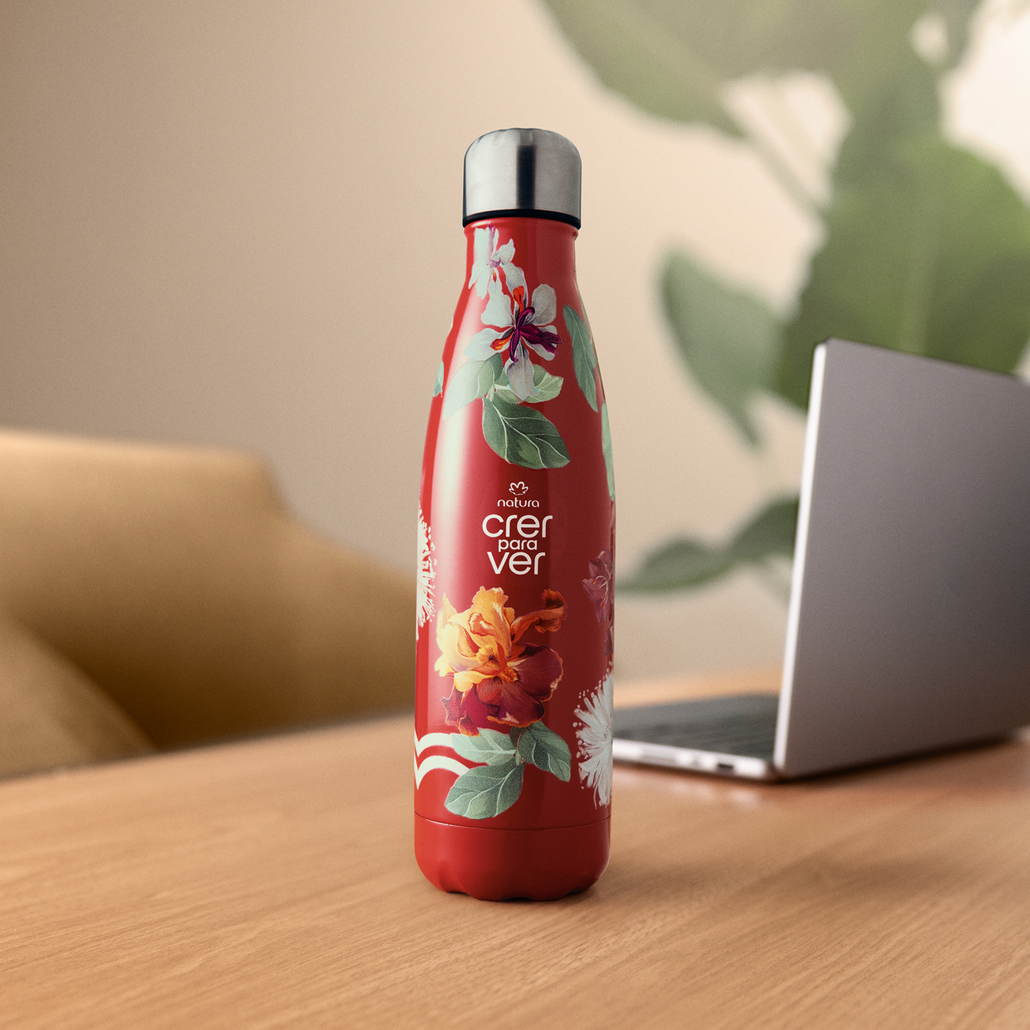 Garrafa Térmica Crer Para Ver na cor vermelho com estampa de flores apoiada sobre mesa de madeira. Fundo desfocado com notebook e cadeira de escritório. 