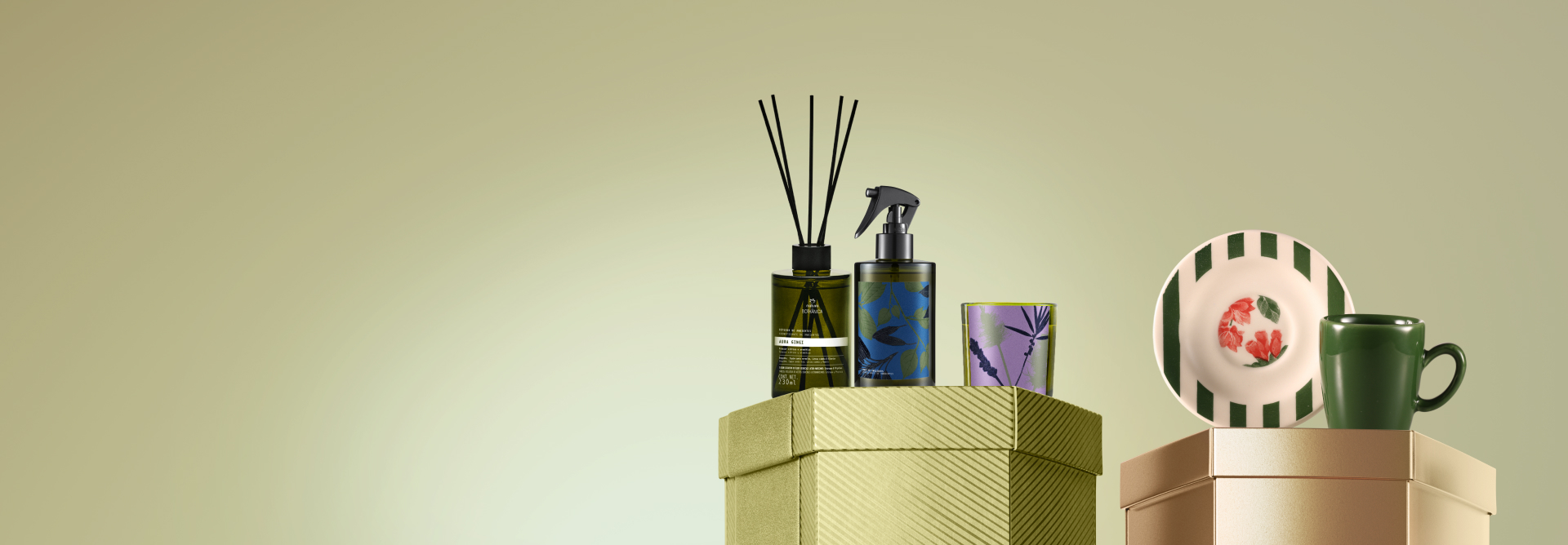 Embalagens Natura sobre caixas brilhantes verde e dourada, em fundo verde: aromatizador de ambientes com varetas, spray de ambientes e vela Bothânica, prato estampado com listras e flores e caneca verde.