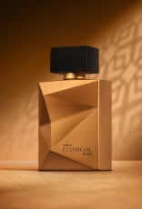 Deo Parfum Essencial Mirra Masculino em frasco facetado dourado com tampa preta. Está em fundo cor areia com sombra geométrica projetada.