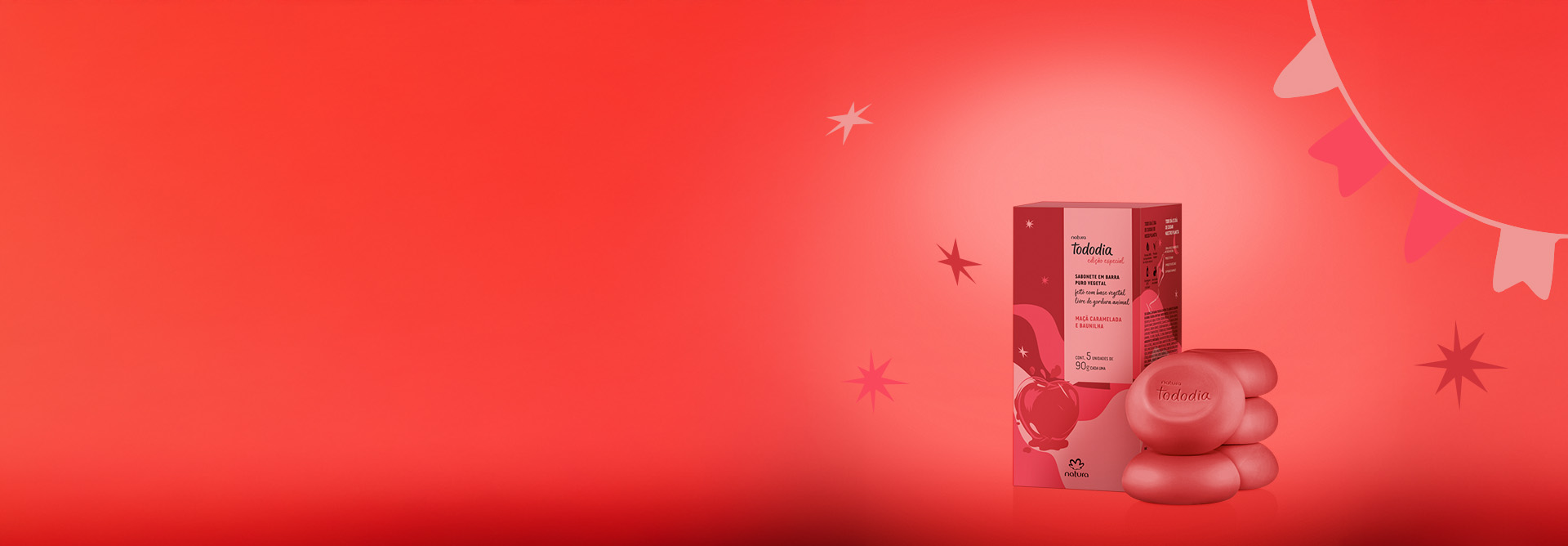 Sabonete em Barra Tododia Maçã Caramelada e Baunilha com 5 barras vermelhas redondas empilhadas ao lado de uma caixa vermelha com ilustração de maçã. Fundo vermelho com estrelas e bandeirinhas.