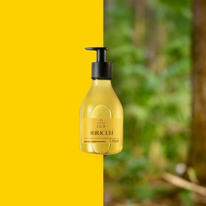 Frasco transparente com pump preto do Sabonete Líquido para Mãos Ekos Maracujá ao centro. Fundo dividido entre amarelo vibrante e floresta desfocada.