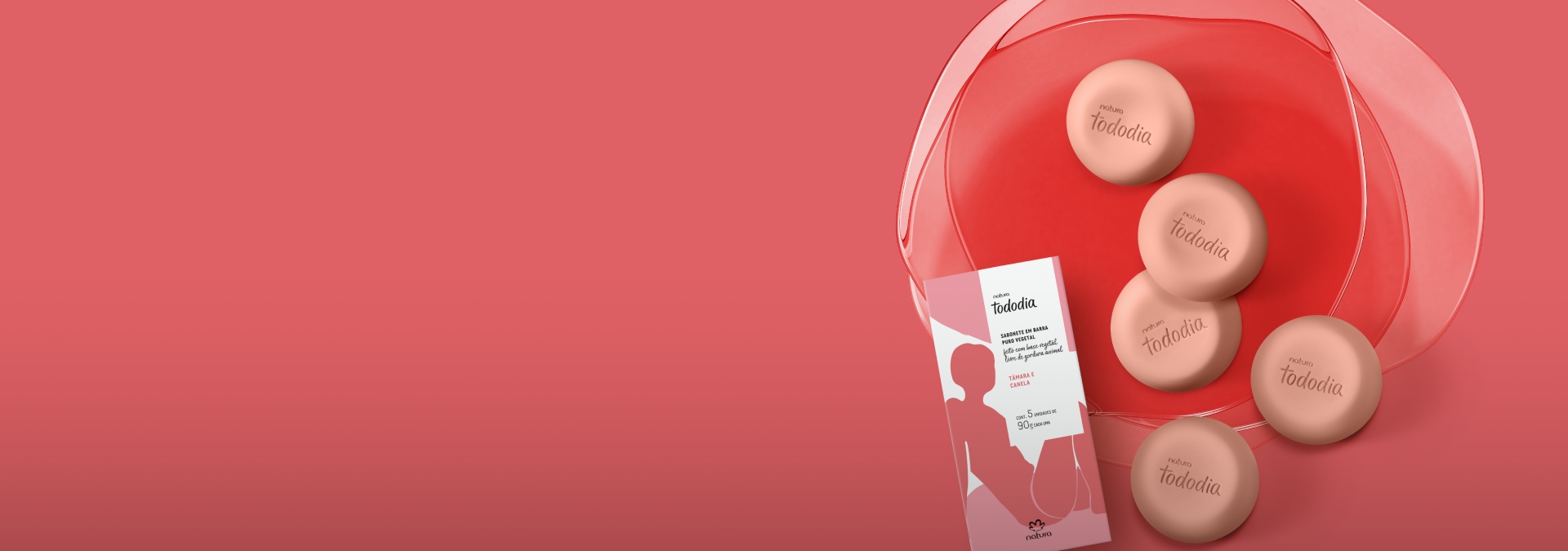 Foto de uma caixa de sabonetes Tododia Tâmara e Canela sobre fundo vermelho. Ao lado da caixa, contém 5 barras de sabonete com formato circular na cor vermelho.