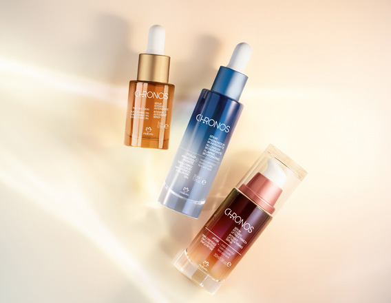 Foto com 3 produtos Chronos, incluindo um Super Sérum Redutor de Rugas, um Sérum Preenchedor Biohidratante e Sérum Intensivo Lifting e Firmeza. Fundo claro com raios de luz.