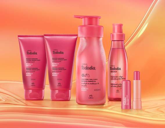 Itens Tododia Acerola e Hibisco, em rosa: bisnagas dos tons de Iluminador, frasco de Creme Sorbet, frasco de Body Splash e embalagem aberta de Balm Labial sobre grafismo e fundo em laranja.