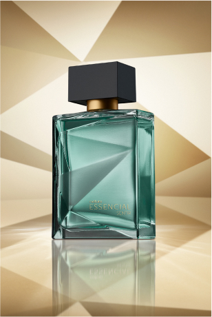 Frasco de Essencial Sentir Masculino, em tom de verde-água e tampa preta, aparece em destaque em fundo dourado multifacetado, fazendo alusão ao design dos frascos de Essencial.