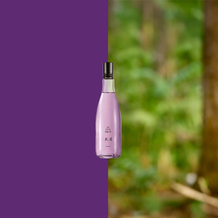 Frasco lilás do Desodorante Colônia Ekos Açaí centralizado, com metade do fundo roxo e metade mostrando floresta desfocada, sugerindo conexão com a natureza.