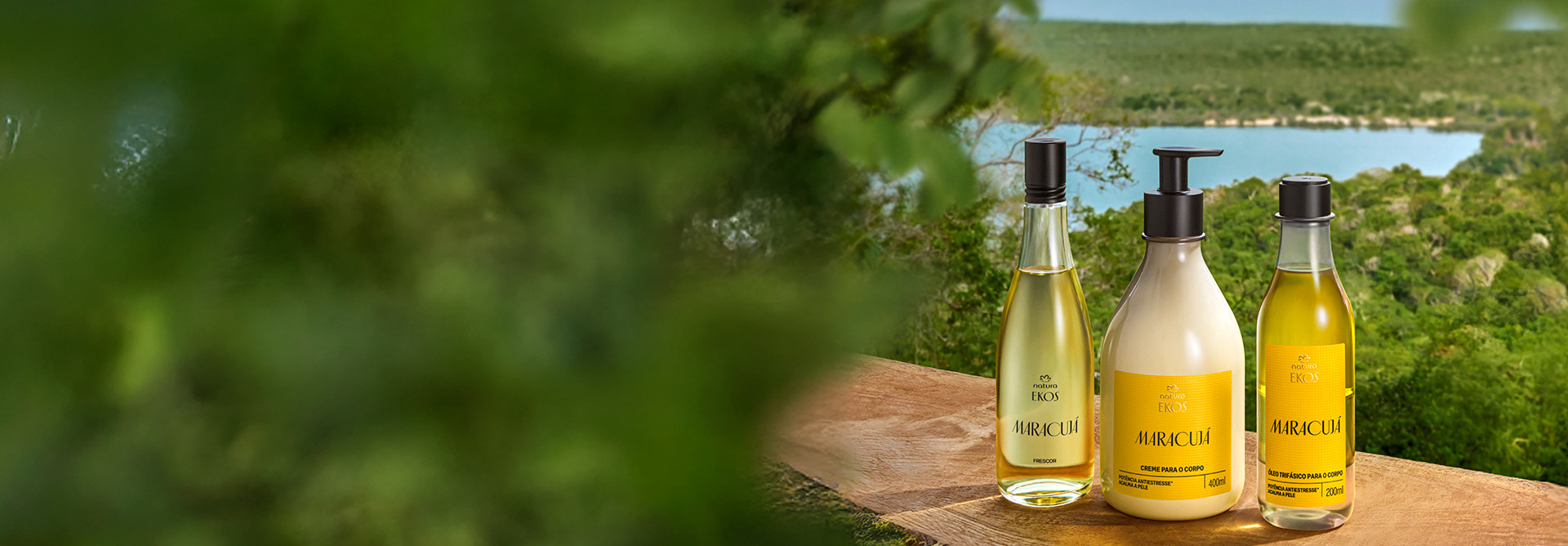 Três produtos de Ekos Maracujá sobre superfície de madeira: Desodorante Colônia Frescor, Creme Desodorante Hidrante para o Corpo e Óleo Trifásico Desodorante Corporal. Ao fundo, vegetação verde e lago.