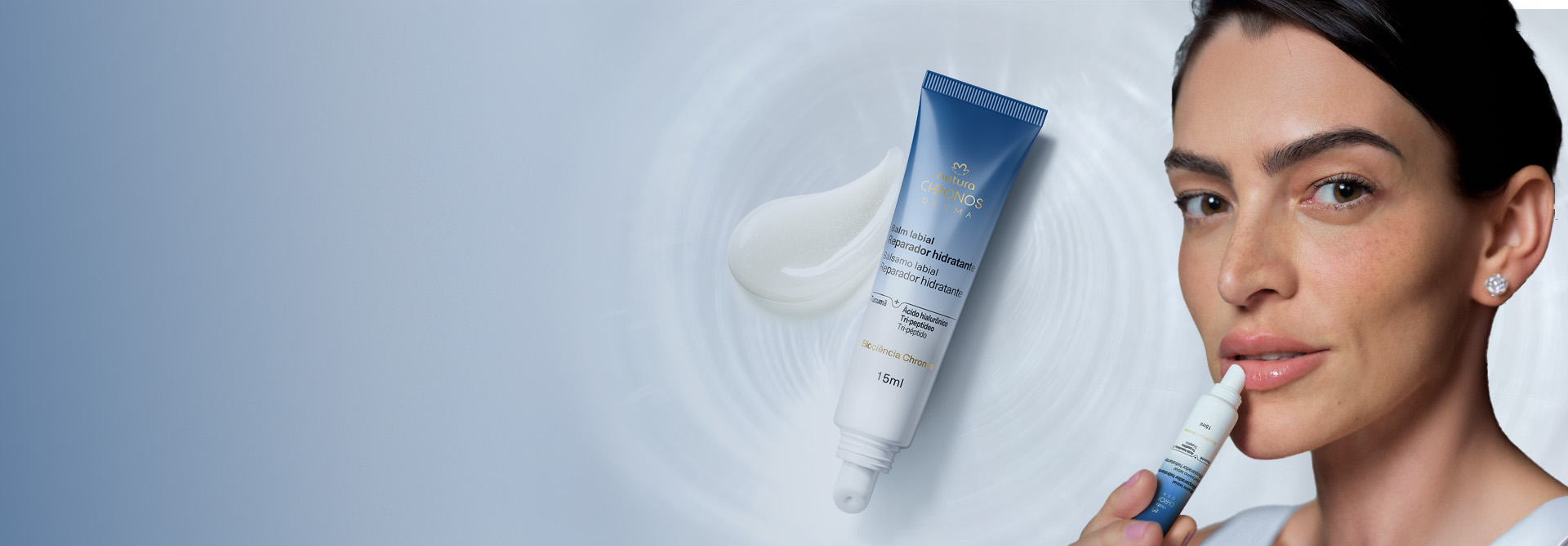 Bisnaga branca com azul do Balm Reparador Hidratante Chronos Derma deitada sobre um pouco de produto com textura cremosa branca. Fundo azul-claro com ondulações.