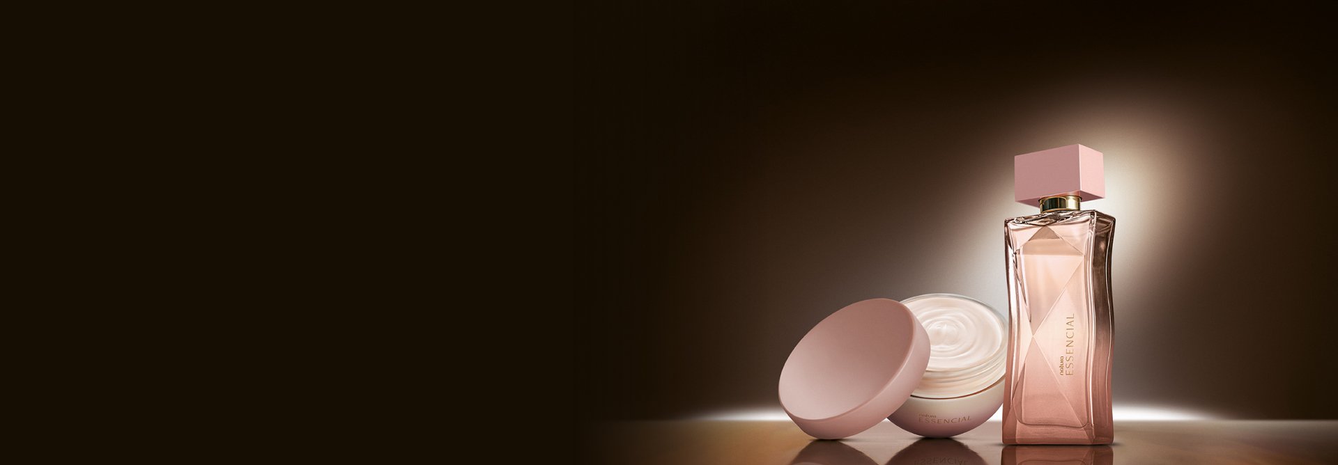 Na cena, Desodorante Hidratante Corporal Perfumado Essencial Feminino e Deo Parfum Essencial Feminino aparecem iluminados sobre superfície marrom em fundo escuro.