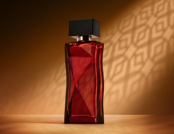 Deo Parfum Essencial Safran Feminino em frasco facetado vermelho com tampa preta. Está em fundo cor areia com sombra geométrica projetada.