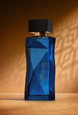 Deo Parfum Essencial Oud Feminino em frasco facetado azul com tampa preta. Está em fundo cor areia com sombra geométrica projetada.