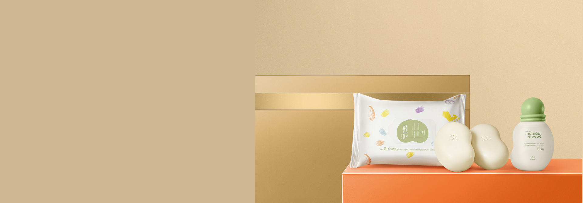 Presente Natura Mamãe e Bebê com embalagem de Lenços Umedecidos, Sabonetes em Barra e Água de Colônia sobre caixa presenteável retangular laranja, em fundo dourado com caixa presenteável dourada.