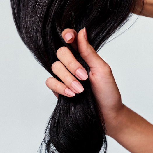 Foto com o detalhe dos dedos de uma mão feminina entre  os fios de cabelos castanhos longos.