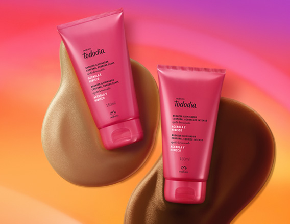 Bisnagas rosa de dois tons de Iluminador Tododia Acerola e Hibisco sobre duas texturas em marrom, claro e escuro, em fundo em tons de amarelo, laranja e rosa.