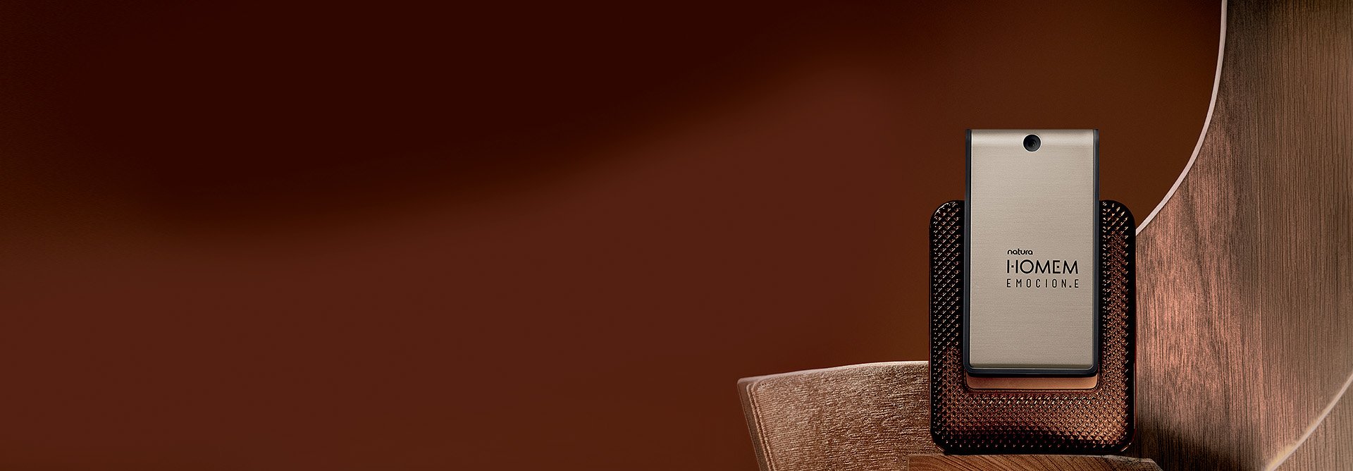 Natura Homem Emocion.e, com frasco de vidro âmbar e centro metálico em tom de bronze destaca-se sobre madeiras retas e curvas. Fundo marrom.
