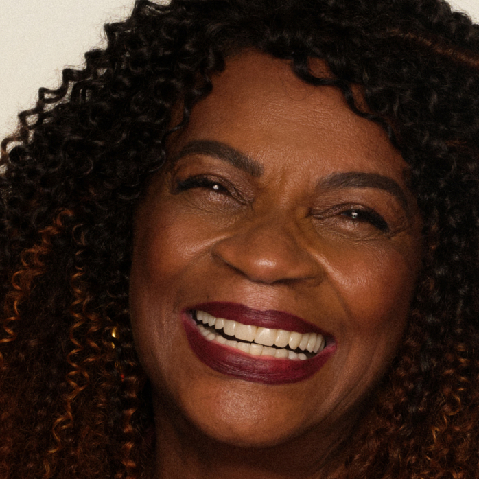 Foto de mulher negra sorrindo com cabelos cacheados e pele madura.