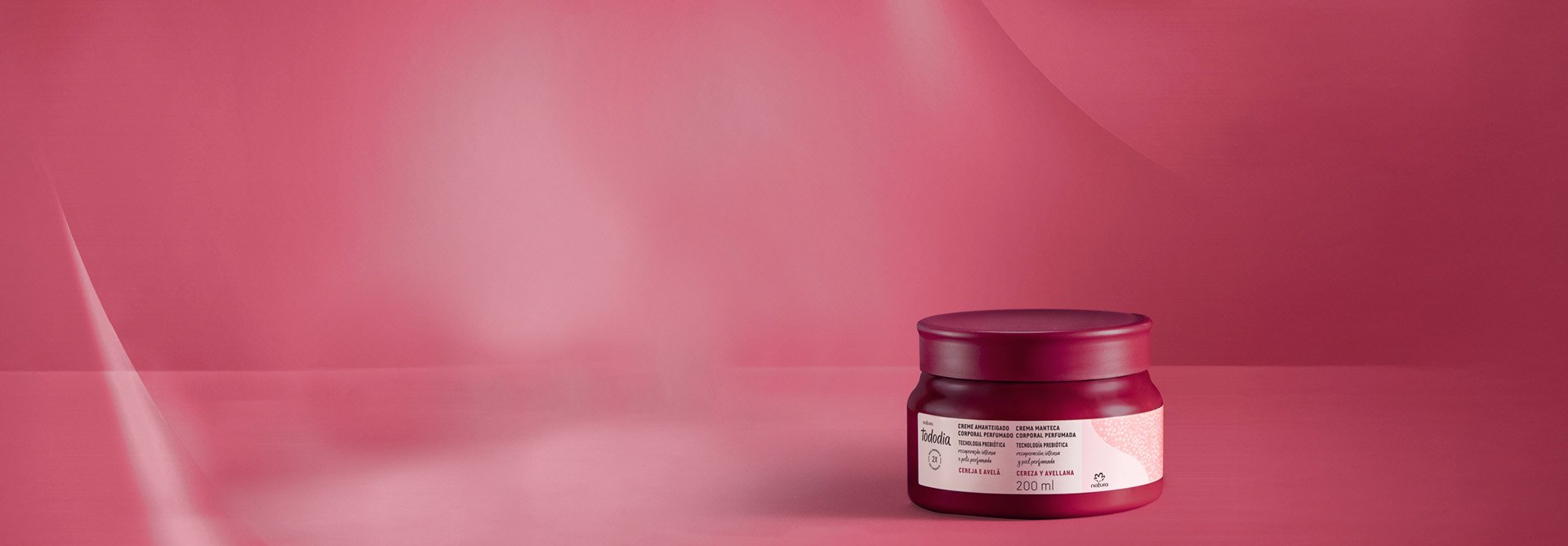 Creme Amanteigado Corporal Perfumado Tododia Cereja e Avelã sobre fundo vermelho. O pote é vermelho com rótulo cor-de-rosa.