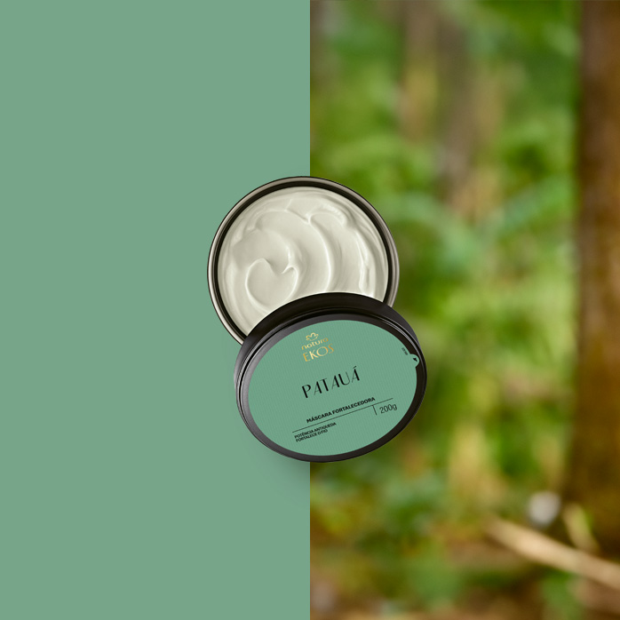 Pote aberto da Máscara Fortalecedora Ekos Patauá, com tampa verde ao lado mostrando o creme branco de textura densa. Fundo dividido entre verde fosco e floresta desfocada.