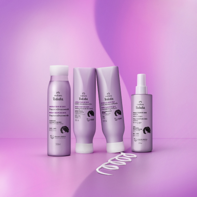 4 produtos de Tododia Cachos e Crespos, incluindo 1 Shampoo, 1 Condicionador, 1 Creme para Pentear e 1 Spray Reativador de Cachos, com embalagens lilazes e tampas brancas, sobre fundo lilás.
