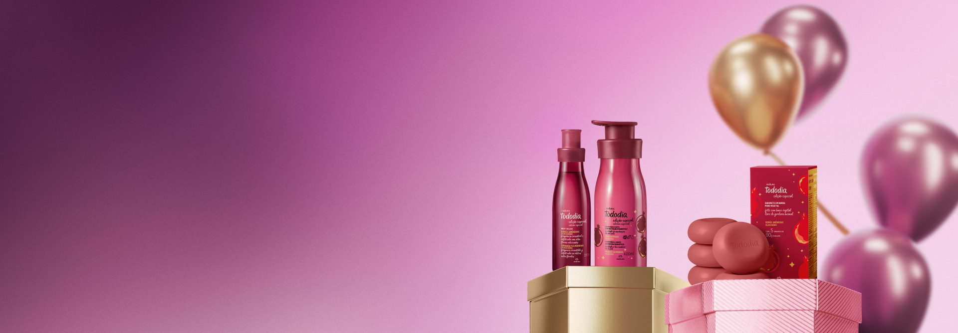 Presente Natura Tododia Româ e Amêndoas Glaceadas, com Creme Nutritivo Corporal, Body Splash e Sabonetes em Barra, destaca-se em caixas hexagonais douradas e rosas. Atrás, balões rosas e dourados em fundo rosa.