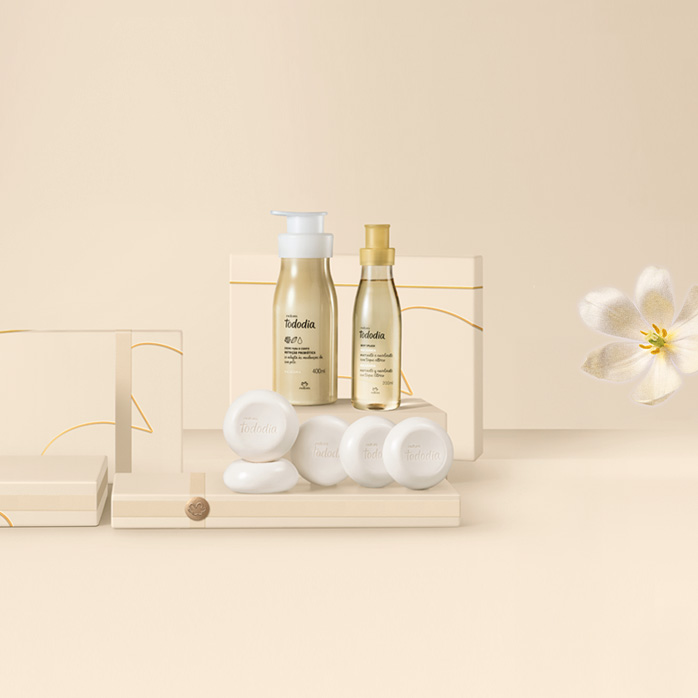 Produtos Natura Tododia Macadâmia sobre caixas presenteáveis e fundo na cor creme com flor branca à direita.