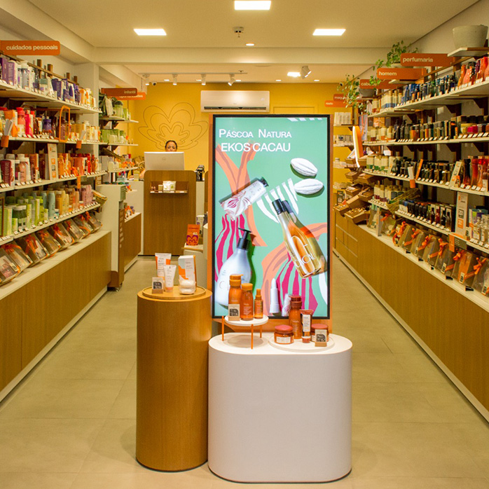Foto da entrada de uma loja Natura com duas bancadas de exposição de produtos e tela Páscoa Natura Ekos Cacau.