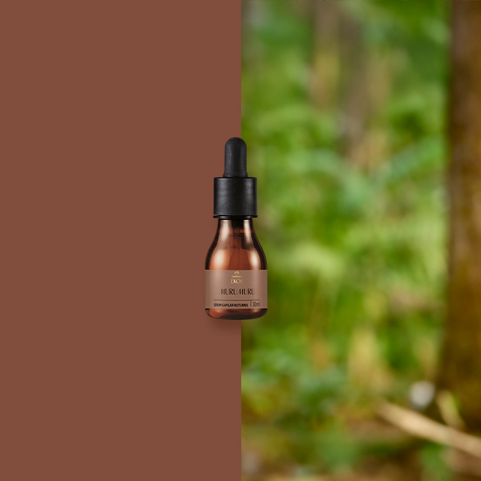 Frasco âmbar do Sérum Noturno Nutritivo Ekos Murumuru com conta-gotas preto ao centro. Fundo dividido entre marrom sólido e floresta desfocada em tons de verde.