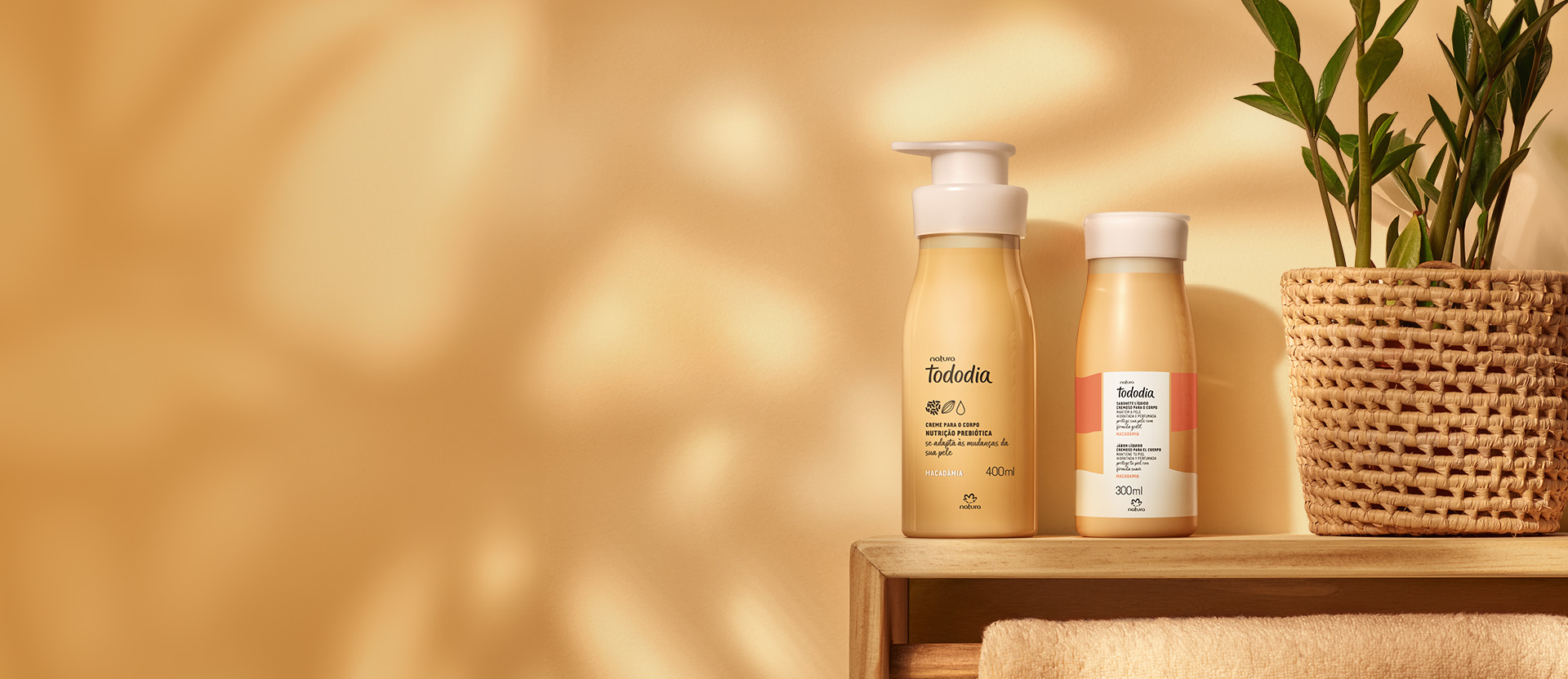 Produtos da linha Natura Tododia sobre móvel de madeira, ao lado de planta, sob luz solar em fundo claro.