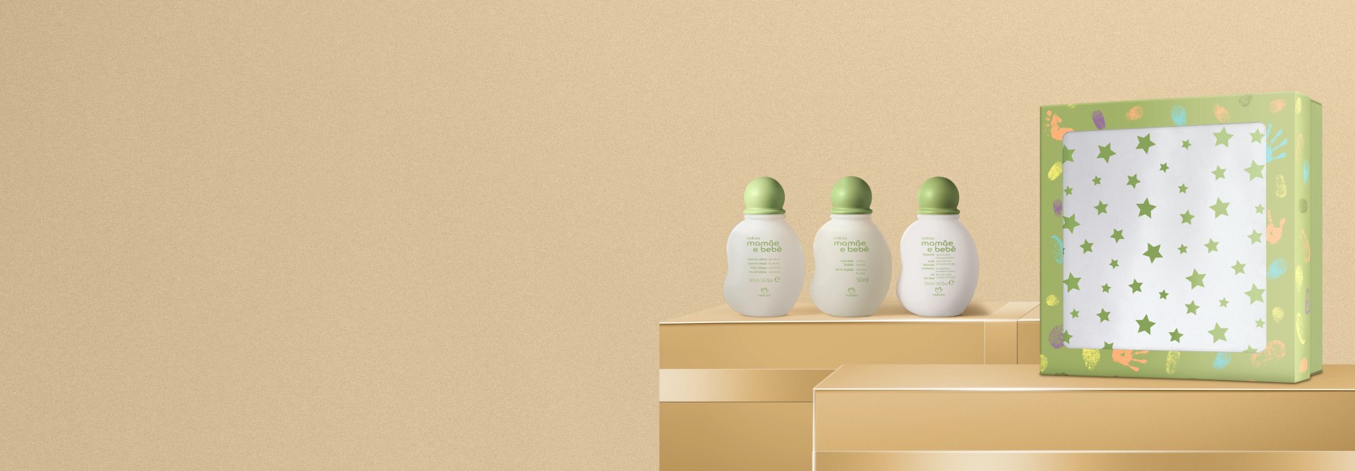 Presente Natura Mamãe e Bebê Miniaturas, Água de Colônia, Hidratante e Sabonete Líquido em fundo dourado sobre caixas com a mesma cor. Frascos brancos com tampa verde ao lado de caixa colorida.
