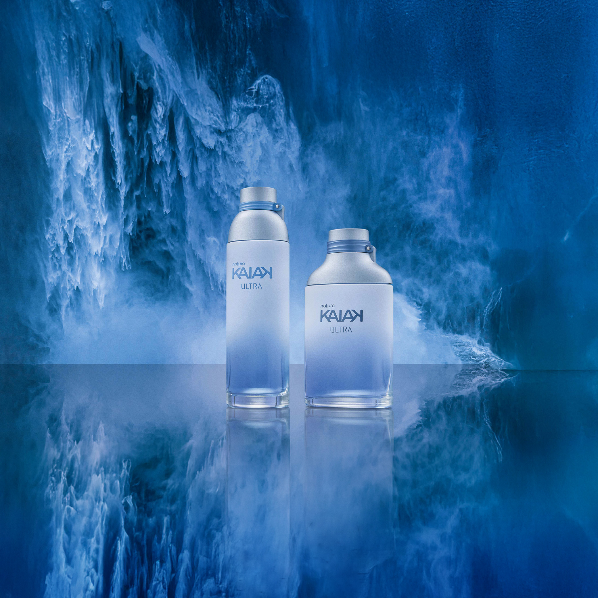Desodorante Colônia Kaiak Ultra Feminino e Desodorante Colônia Kaiak Ultra Masculino em destaque diante de um fundo azul que lembra o mar. Frascos degradê azul com tampa prata.