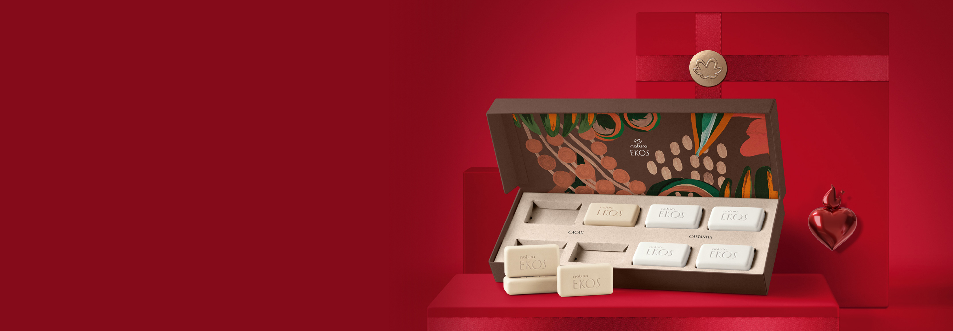 Caixa de sabonetes de Ekos Castanha com 8 unidades. A caixa é marrom com ilustrações de castanhas. Fundo vermelho com caixas de presentes.