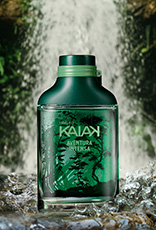 Frasco de Kaiak Aventura Intensa masculino em verde sobre pedras na frente de uma cachoeira cercada por folhagens.