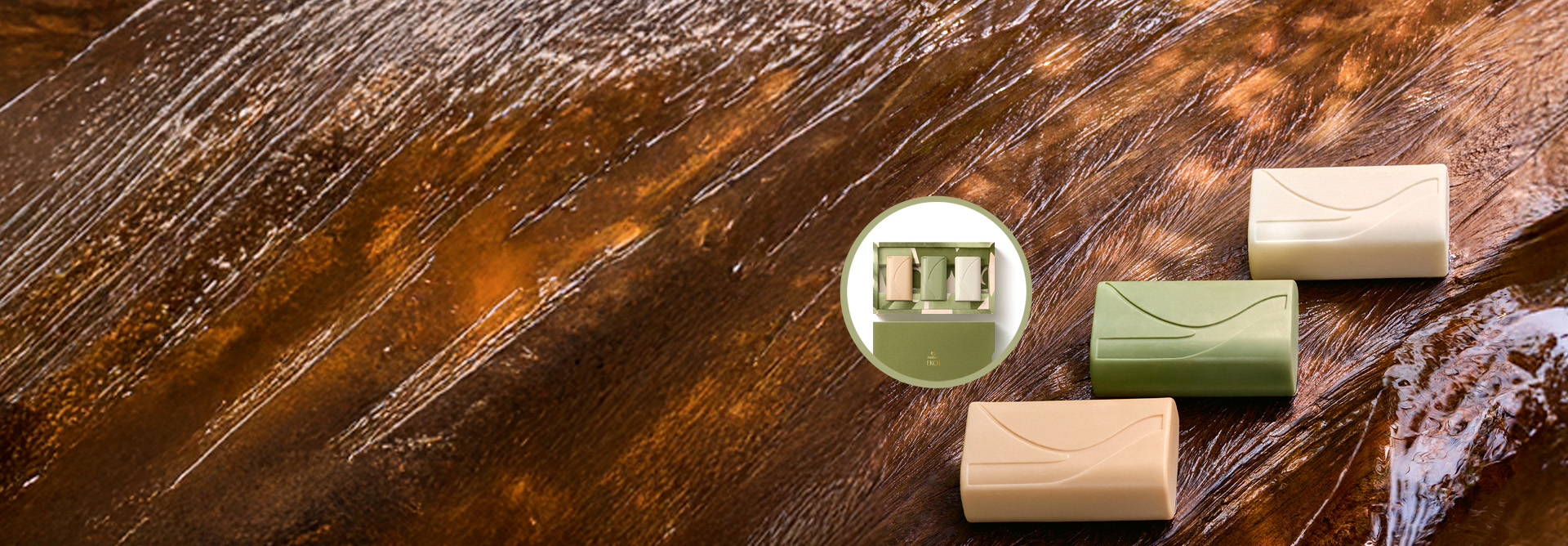 Três Sabonetes Natura Ekos Ryos, em tons bege, verde e branco, estão sobre uma superfície de madeira molhada. No centro, há um detalhe em círculo mostrando a caixa de presente com os três sabonetes.