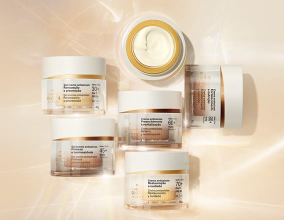 Foto de 6 frascos de Creme Antissinais Chronos Derma, incluindo produtos para diferentes idades. Os potes estão sobre fundo claro com raios de luz. 