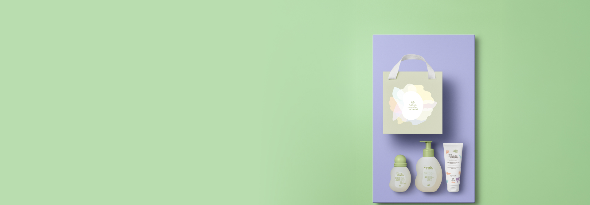 Presente Natura Mamãe e Bebê, incluindo 1 Água de Colônia, 1 Sabonete Líquido, 1 Creme Preventivo de Assaduras e 1 Sacola Presenteável em destaque sobre retângulo lilás em fundo verde-claro.