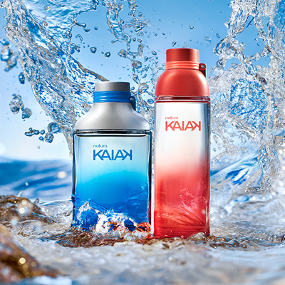 Frascos Natura Kaiak, masculino em azul, e feminino em laranja. Fundo com água e respingos formando ondas.