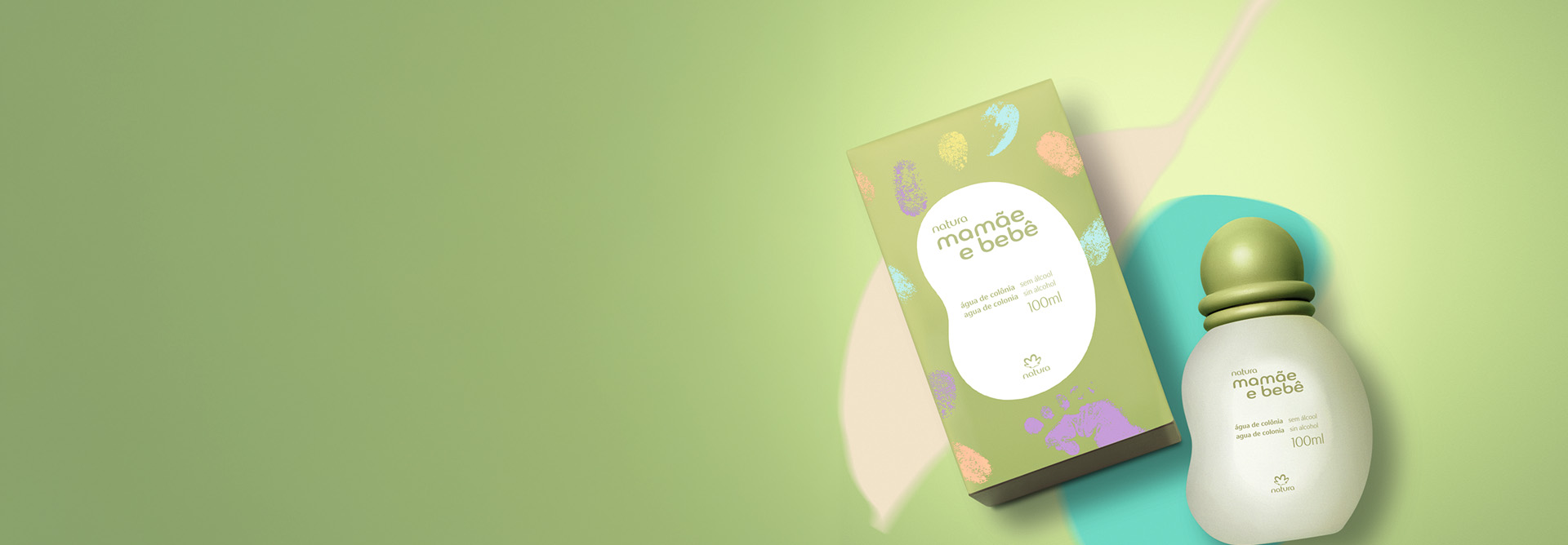 Água de Colônia Natura Mamãe e Bebê, com frasco arredondado branco e tampa verde, aparece ao lado de sua respectiva caixa em fundo verde-claro com nuances em tons de rosa, rosa-claro e azul.