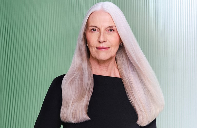 Foto de mulher com cabelo platinado liso e blusa preta, em fundo verde e branco com textura vertical.