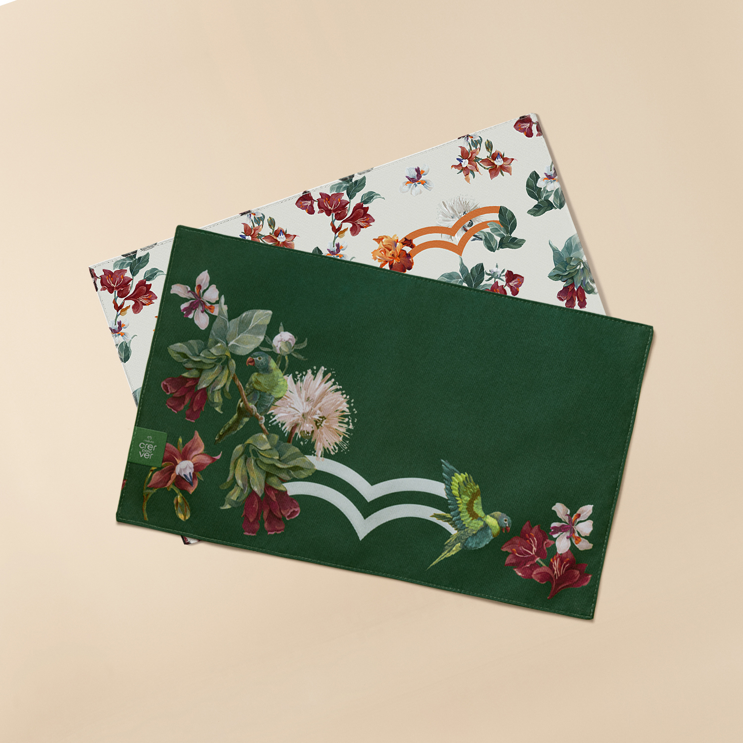 Jogo americano Crer Para Ver com destaque para os dois lados estampados do produto. Um lado é verde escuro e outro branco. Ambos têm estampa floral colorida em tons de laranja, vermelho e branco. 
