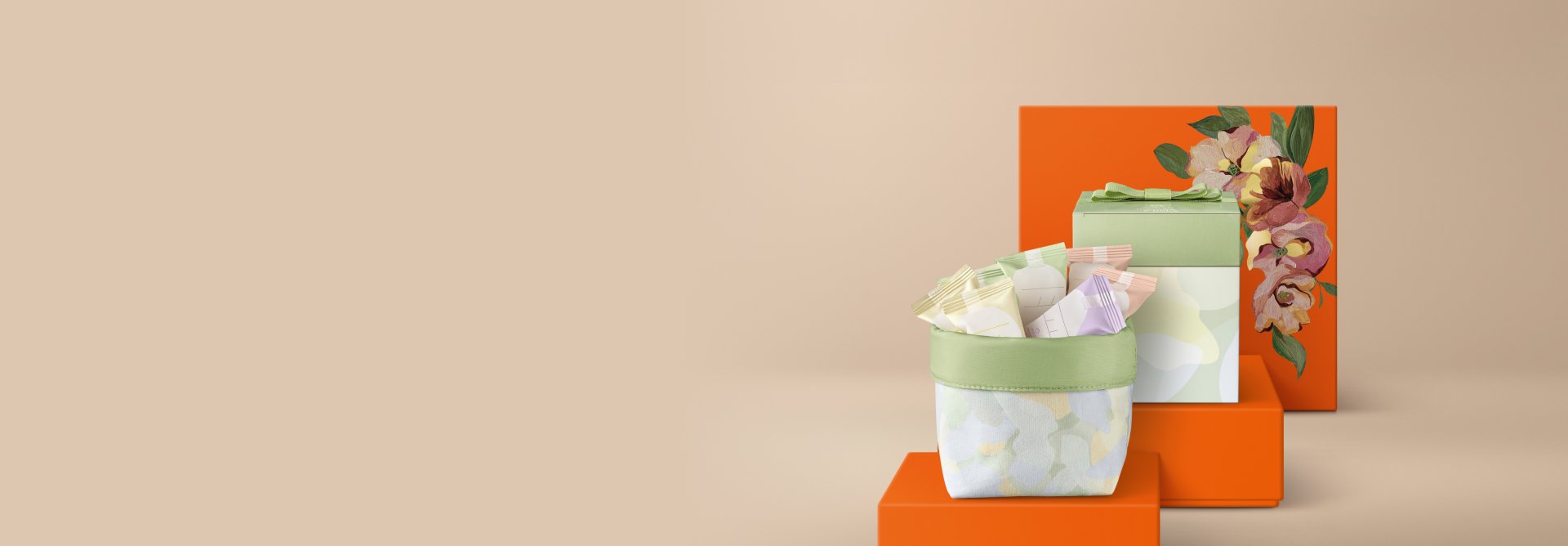 Presente Natura Mamãe e Bebê, contendo 1 Caixa com 20 Minissabonetes e uma cesta de tecido com estampa floral. Os itens estão sobre caixas de presentes laranja com estampa de flores.