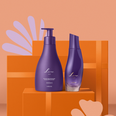 Hidratante Corporal e Desodorante Colônia Luna Nuit Feminino sobre caixas de presente retangulares laranja, em fundo laranja-claro, com ilustrações de flores lilás e alaranjadas.
