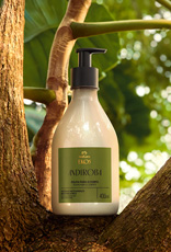 Frasco creme com válvula preta de Polpa Desodorante Hidratante para o Corpo Ekos Andiroba sobre tronco de árvore, em cenário de floresta desfocada.