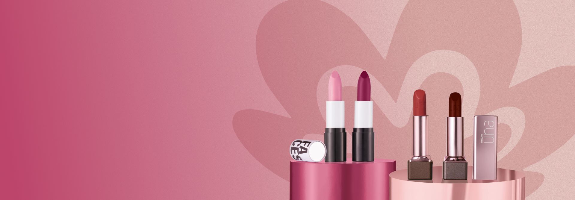 2 batons de Faces e 2 batons de Una, todos em tons de rosa, estão abertos sobre pedestais cilíndricos. Fundo degradê rosa com a flor símbolo da Natura em tom mais escuro. 