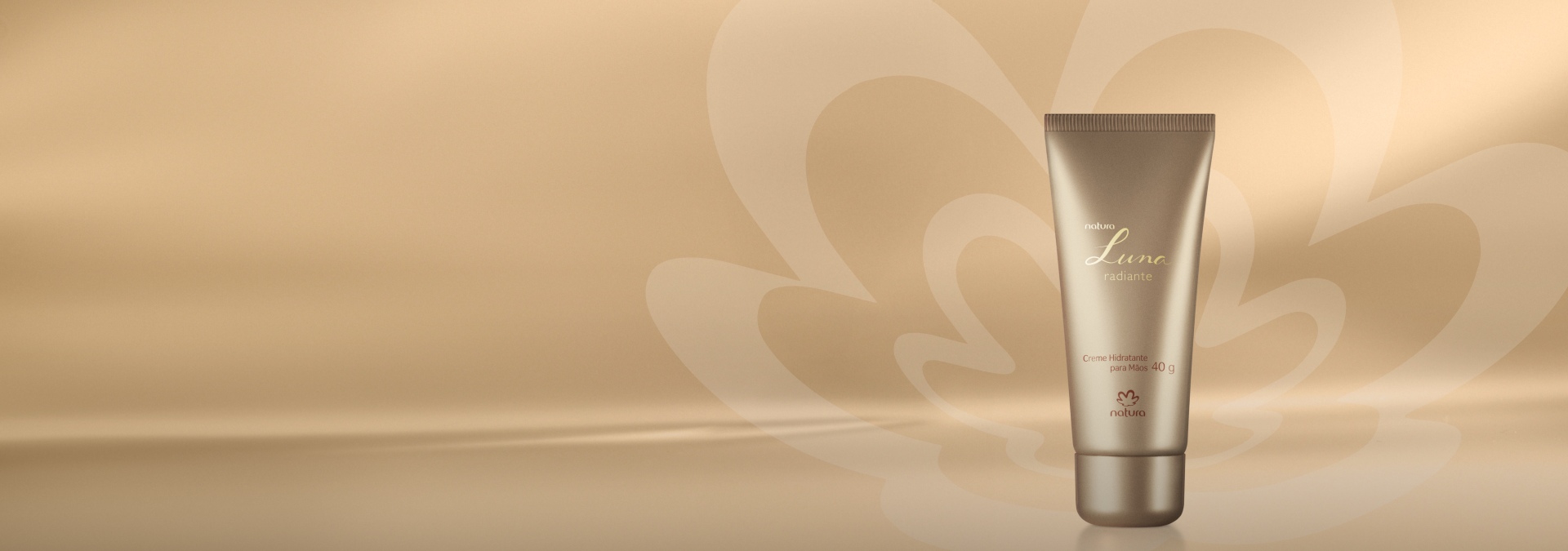 Foto do Creme Hidratante para Mãos Luna Radiante sobre fundo dourado com a flor estilizada da Natura. O frasco do produto é em formato de bisnaga na cor dourado.