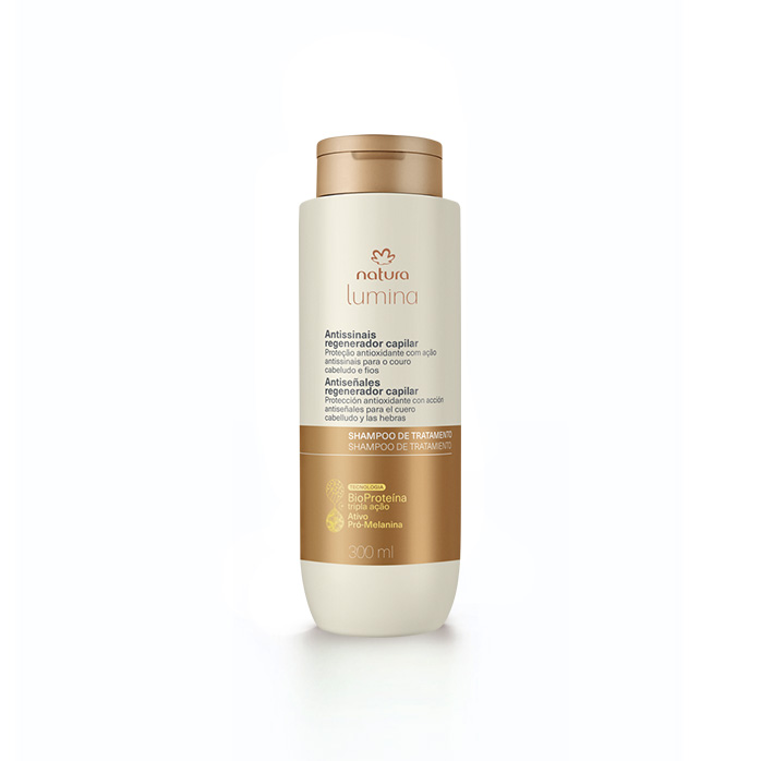 Embalagem creme com tampa e rótulo dourados de Shampoo de Tratamento Antissinais Natura Lumina. Fundo em verde com listras verticais.