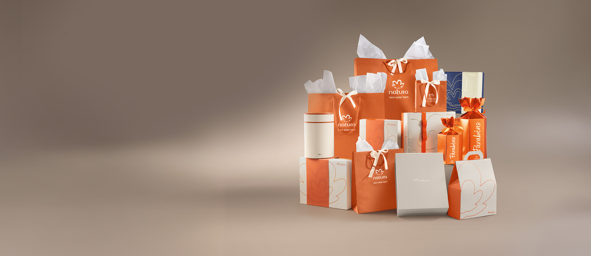 Diversas embalagens de presente Natura, incluindo sacolas, caixas e envelopes. As peças apresentam a flor símbolo da Natura, laços decorativos e variações de cores.